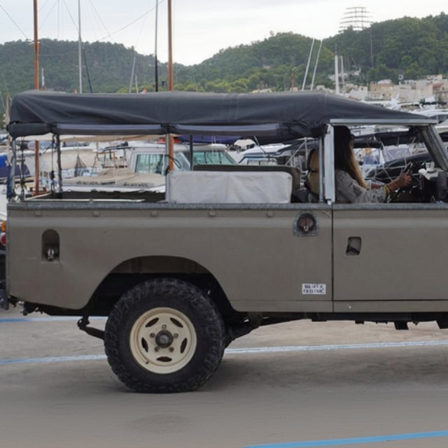 Vintage Land Rover Series III parked in a marina with boats in the background