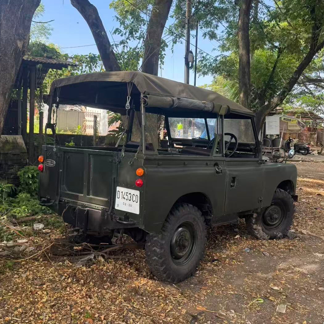 Vintage military-style jeep parked on a dirt road with trees in the background