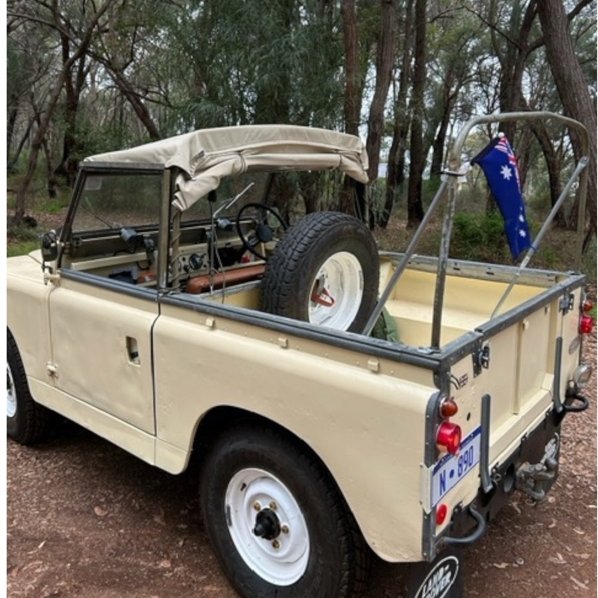 Beige off-road vehicle with open top and Australian flag in a forest setting