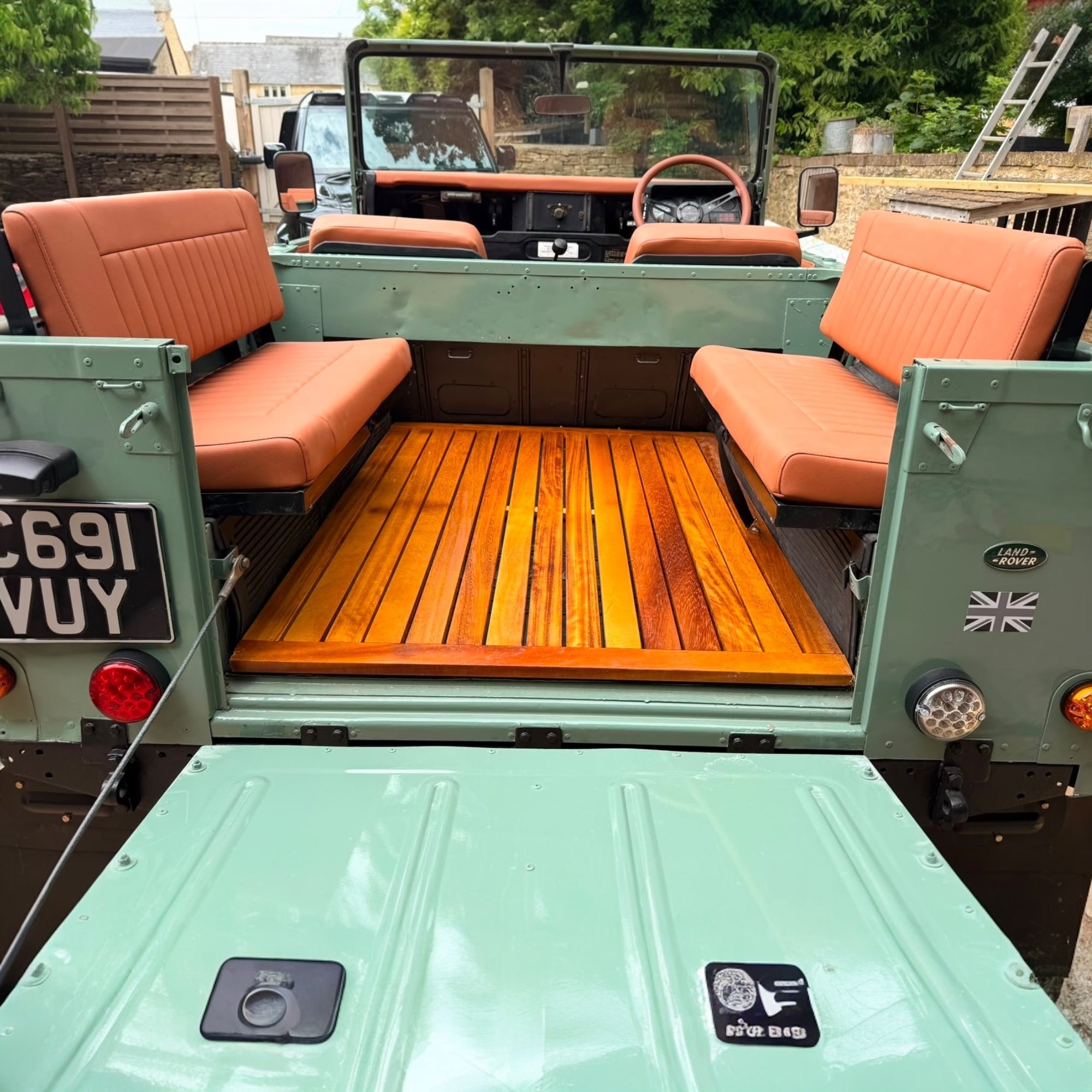 Vintage green jeep with orange seats and wooden floor, parked outdoors.