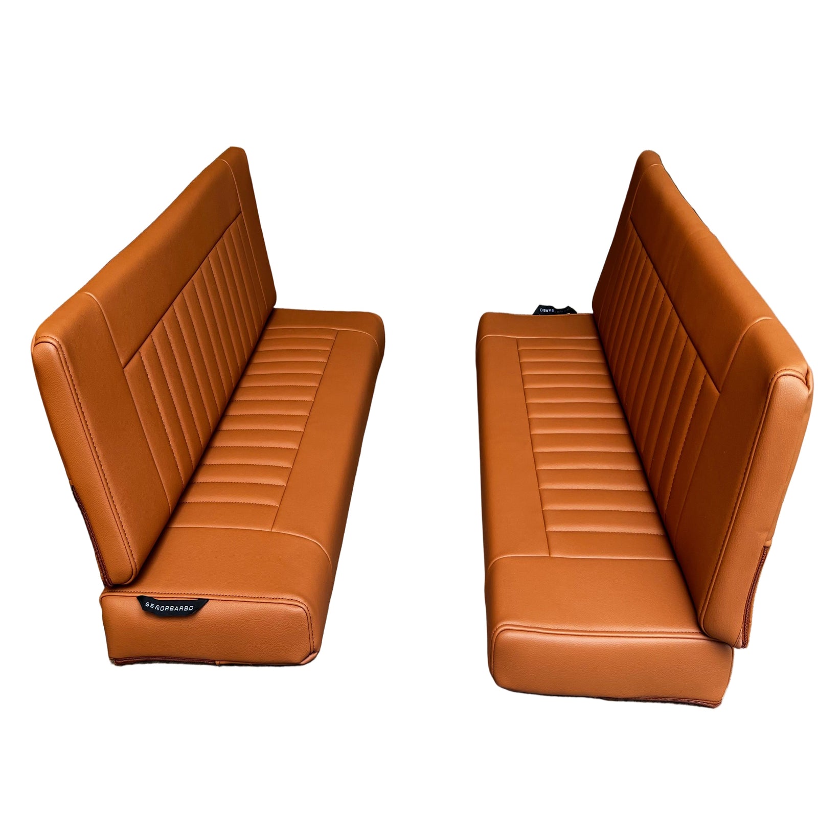 Two brown leather car seats on a concrete floor against a wooden wall.