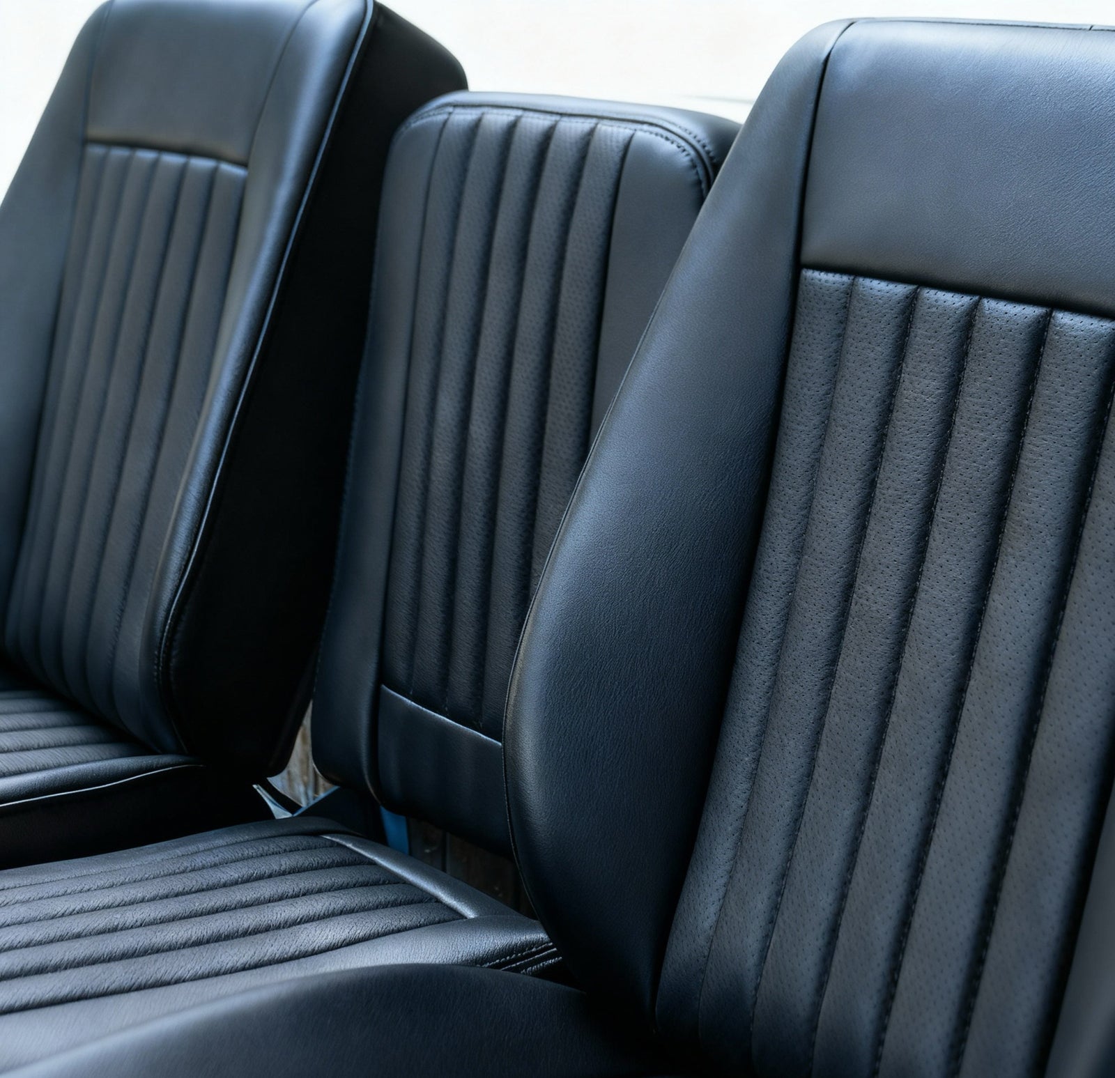 Close-up of three black leather car seats with visible stitching.