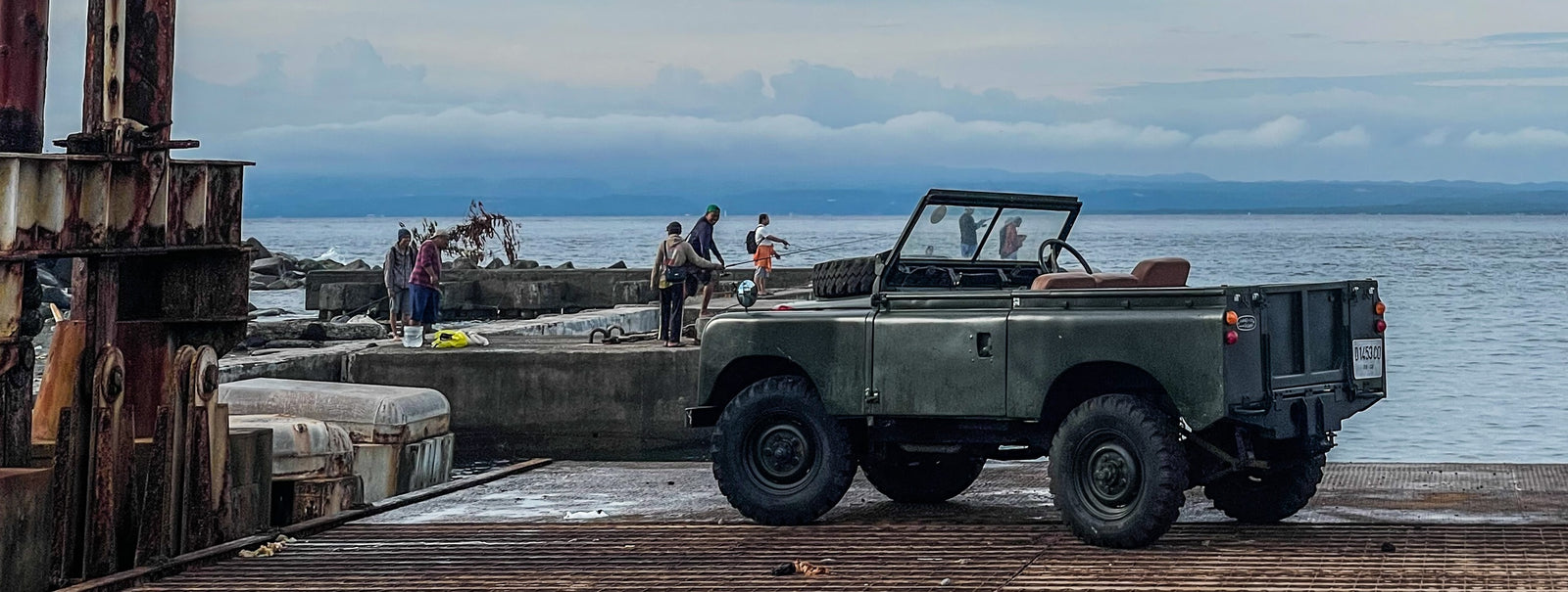 Green off-road vehicle on a dock with people in the background