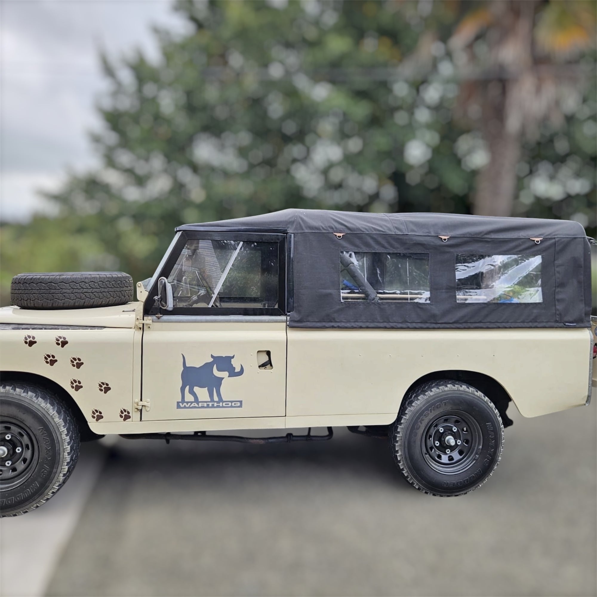 Beige off-road vehicle with a black cover and WARDUR logo on a blurred natural background