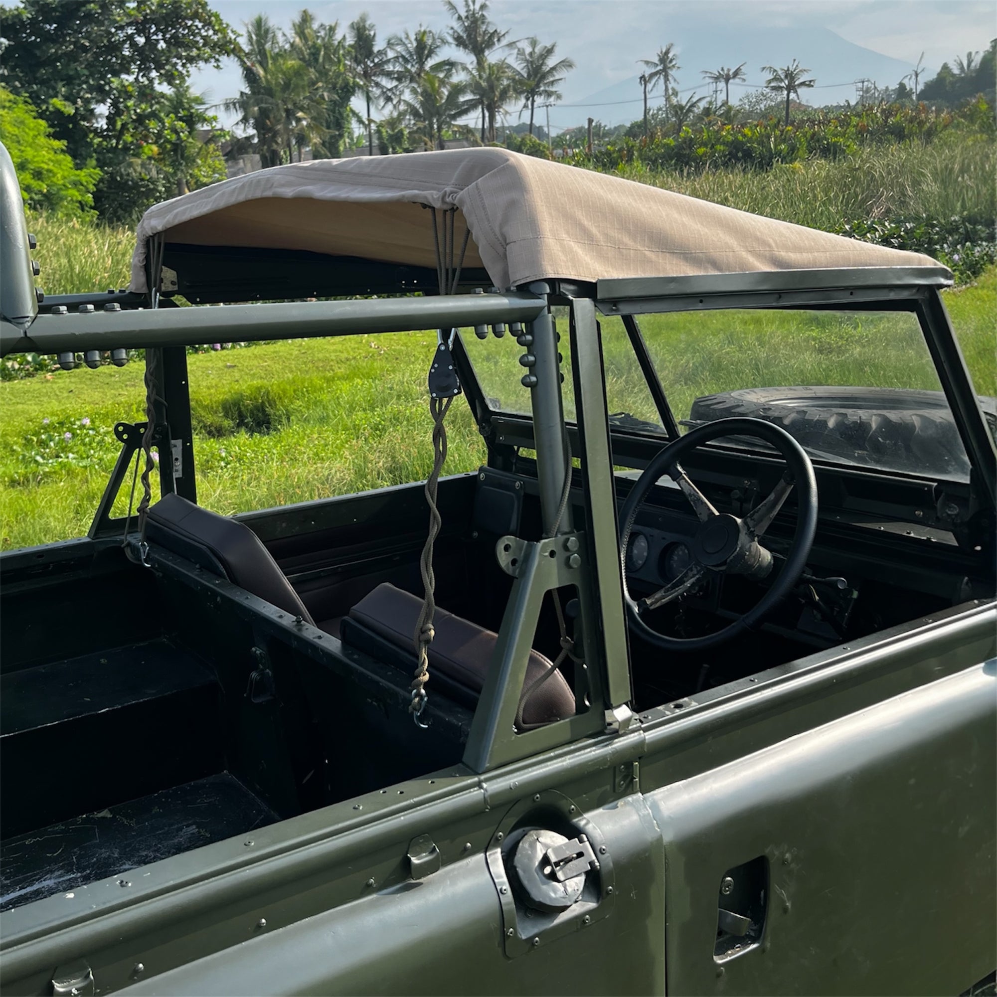 Vintage military-style vehicle with a beige roof in a grassy field