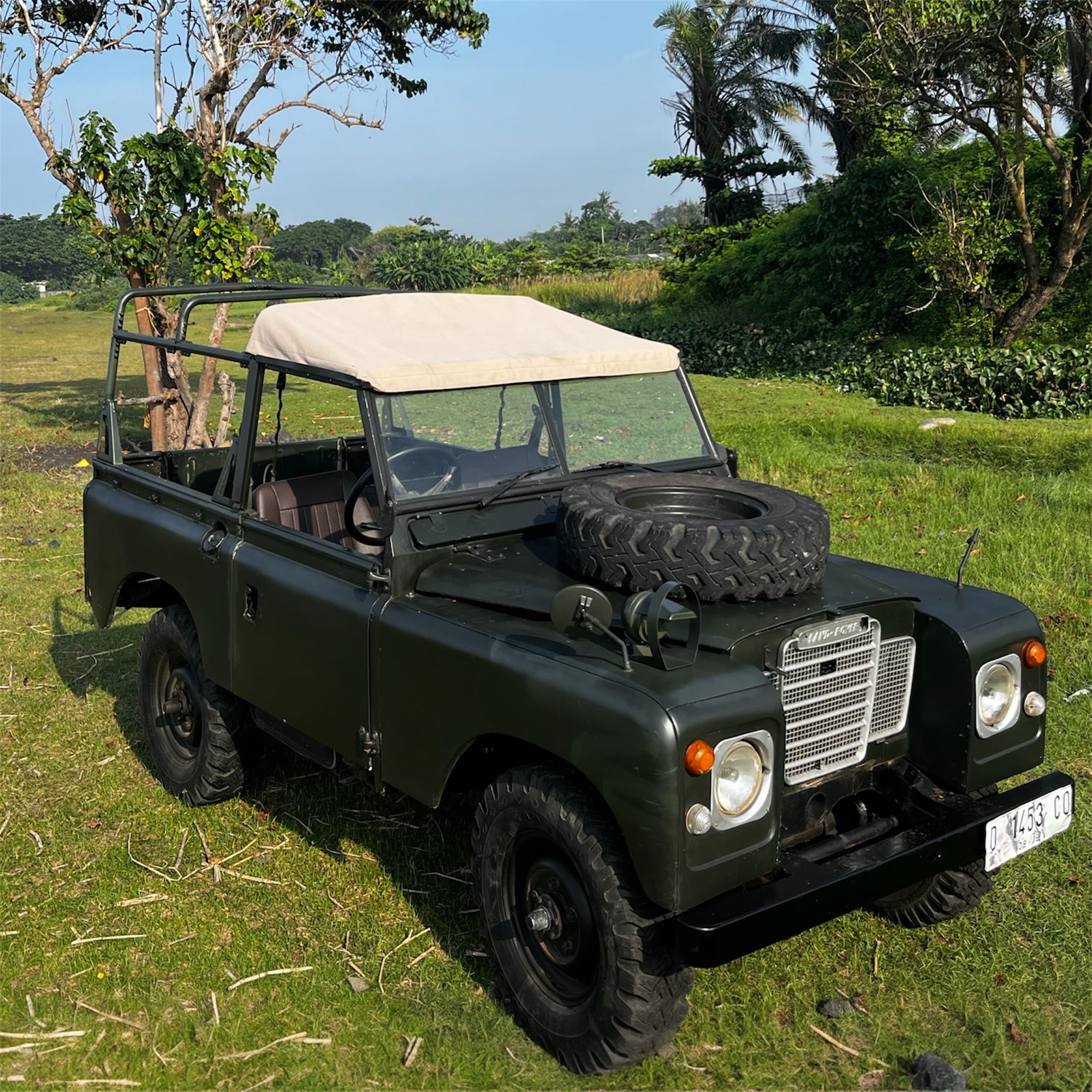 Vintage green jeep with a beige soft top on grassy terrain