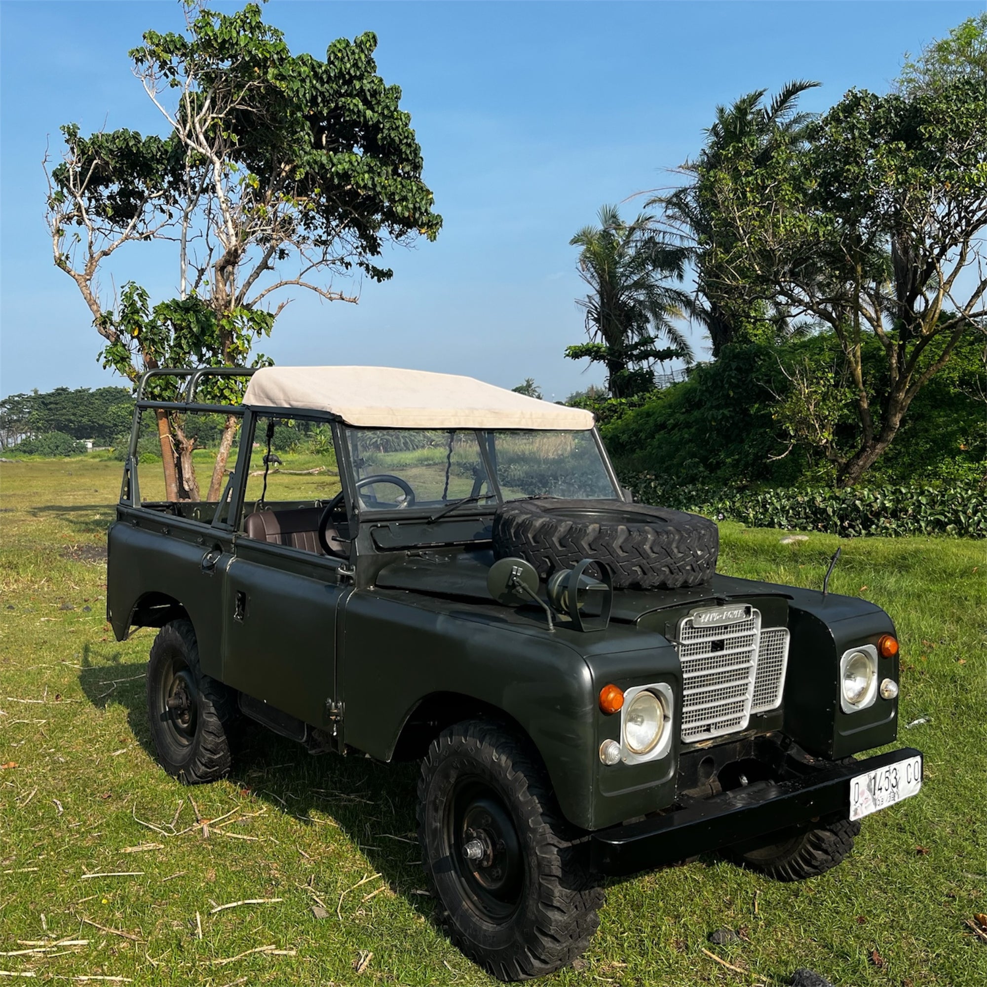 Vintage green jeep in a grassy field with trees in the background