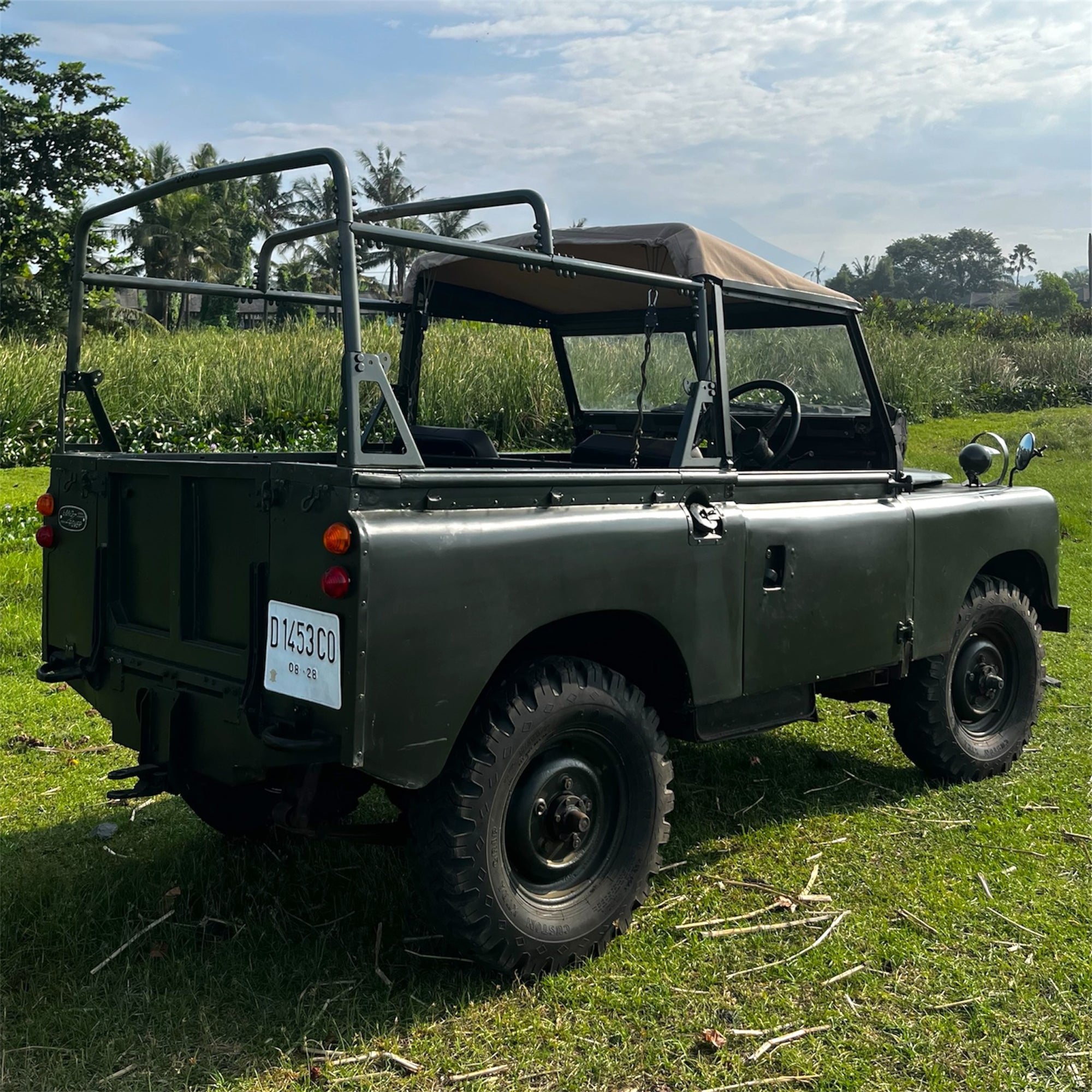 Vintage green jeep in a grassy field with trees in the background