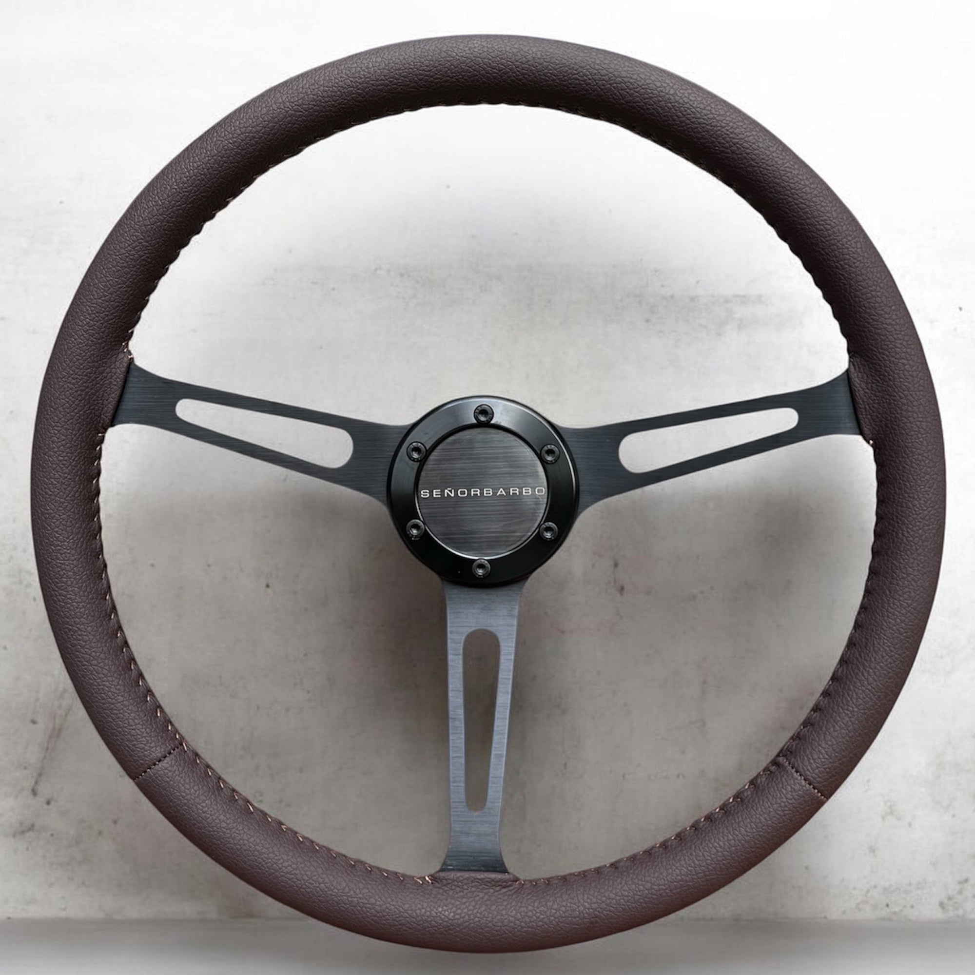 Steering wheel with brown leather cover and silver center on a light gray background