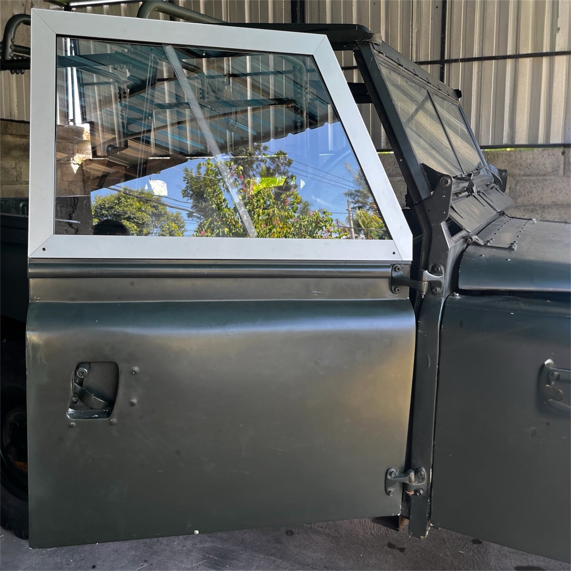 Metallic vehicle door with glass panel and wiper, against a reflective surface.
