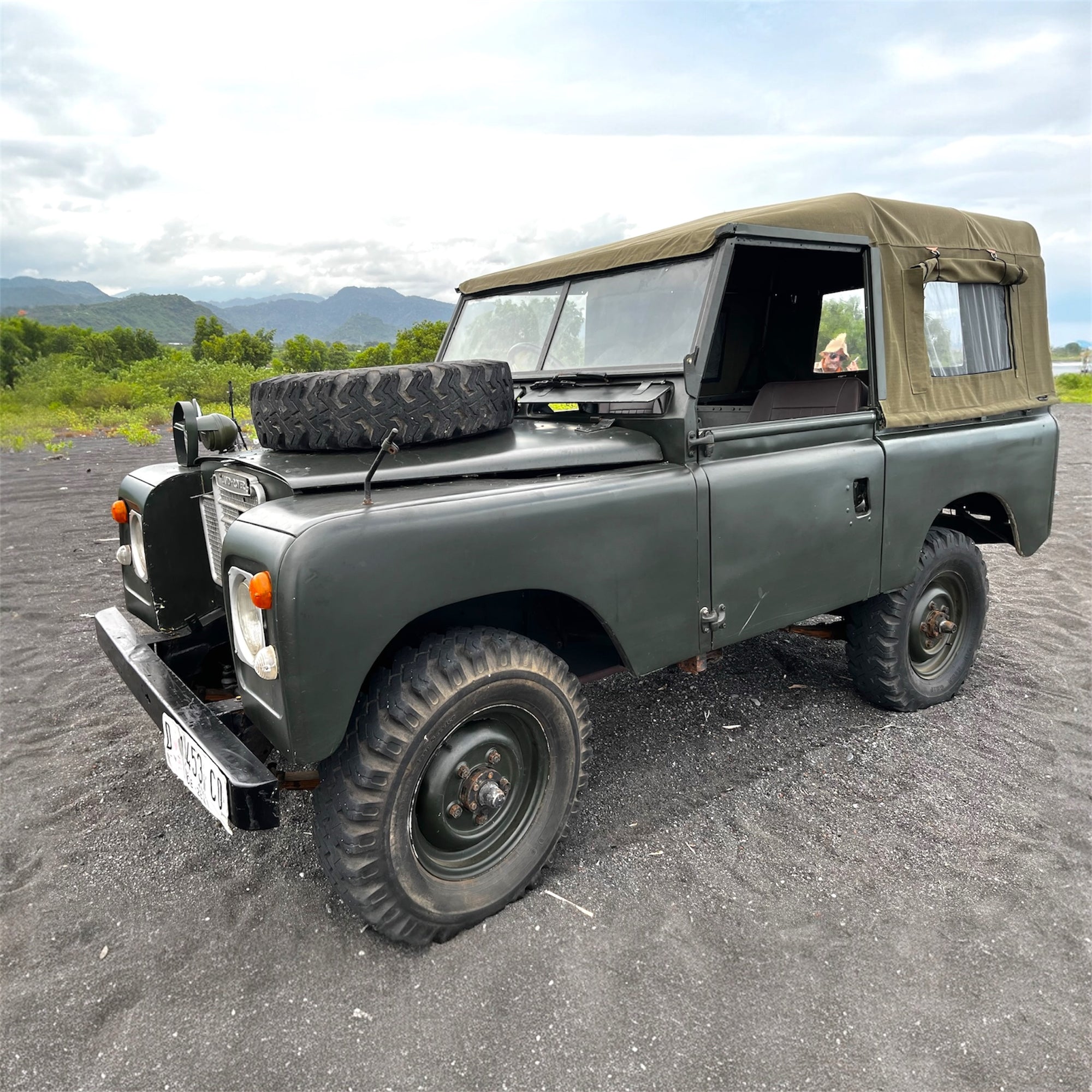 Vintage green jeep with a soft top on a road with mountains in the background