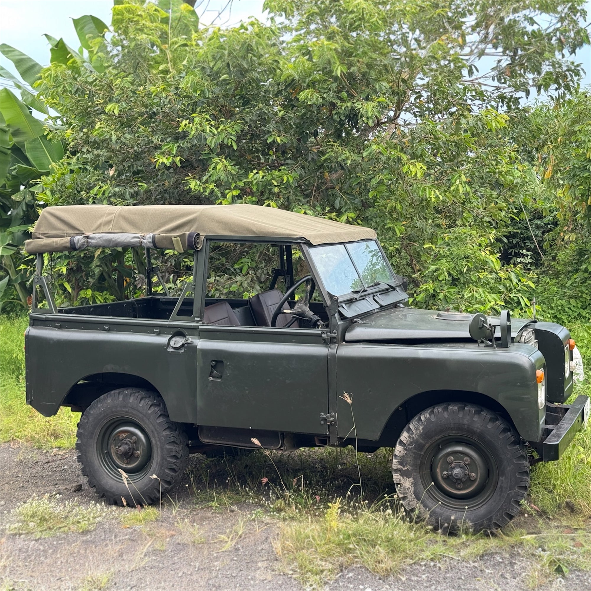 Green off-road vehicle parked on a dirt path with greenery in the background