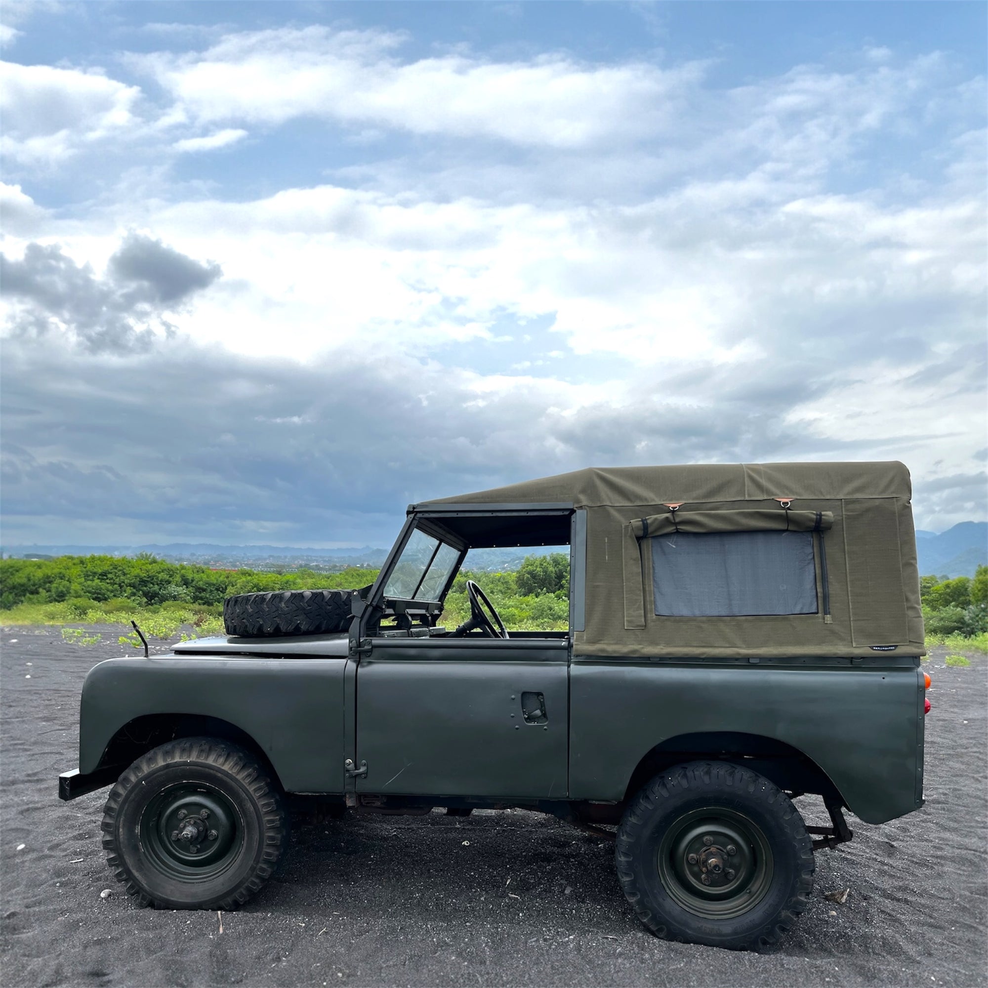 Green vintage jeep on a road with a cloudy sky