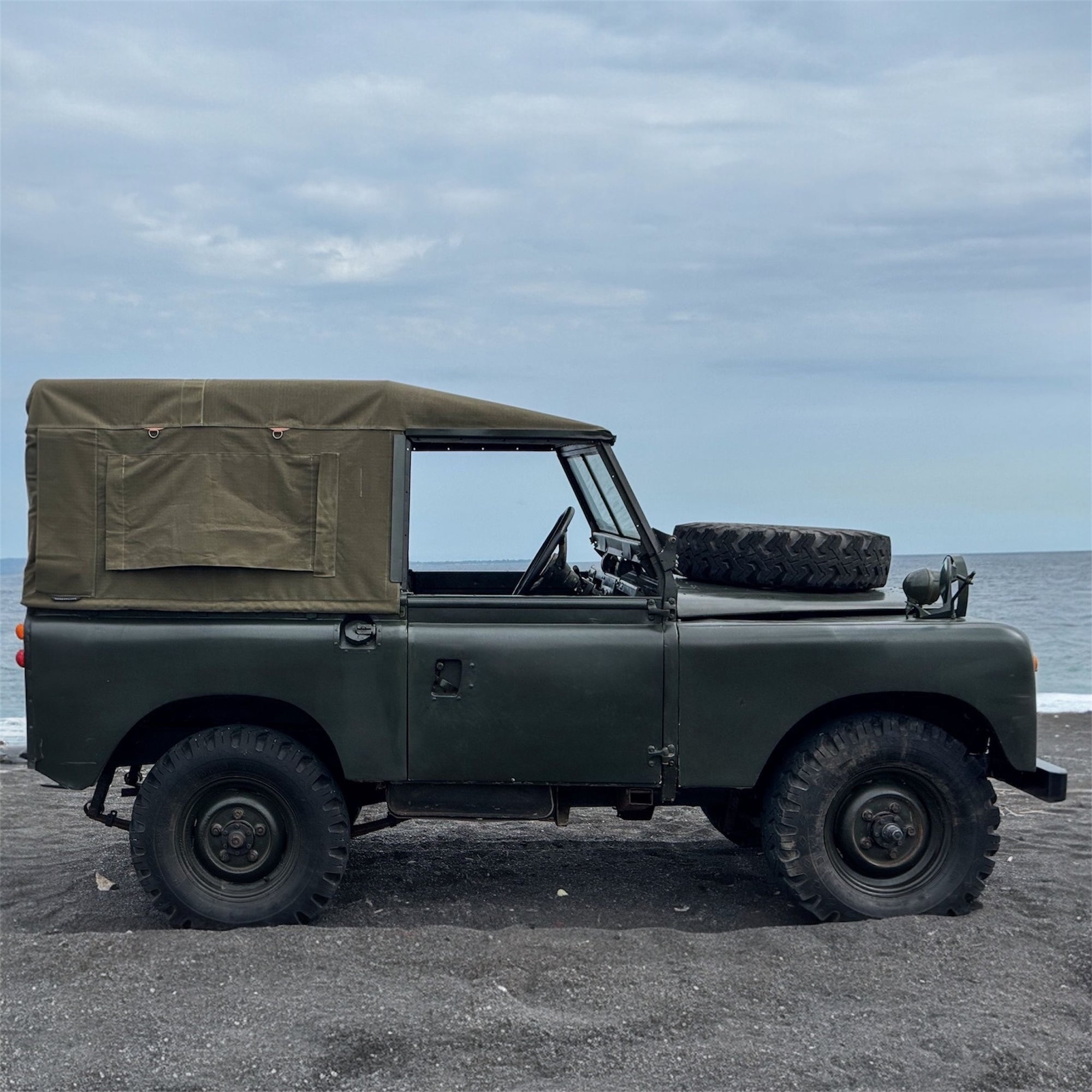Green vintage jeep on a beach with ocean and sky in the background