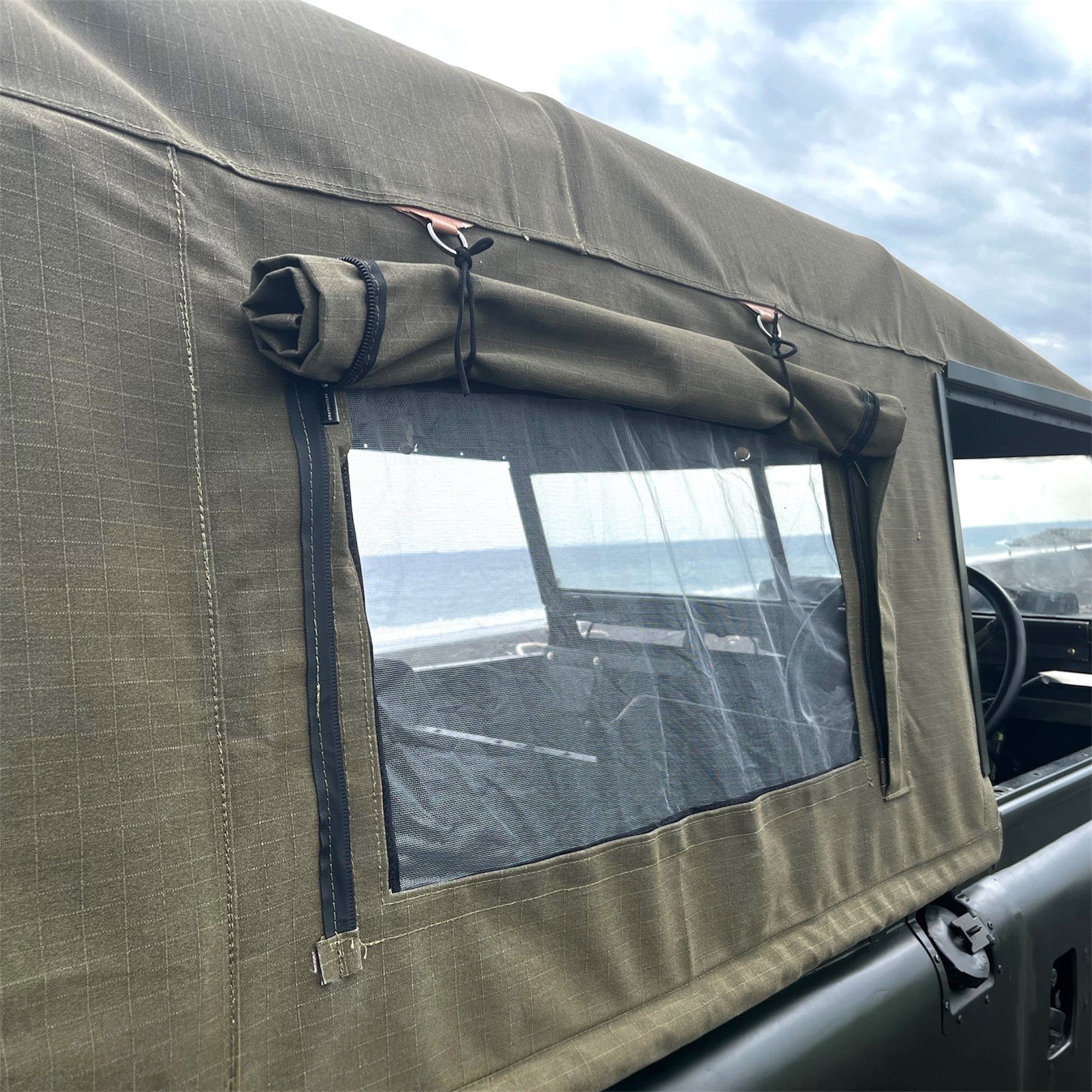 Brown vehicle canopy with window overlooking a beach and ocean.